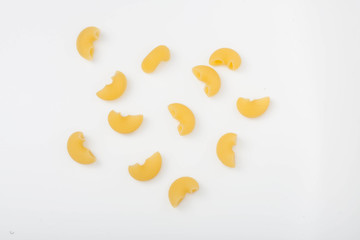 elbow shaped uncooked pasta pieces scattered on white background