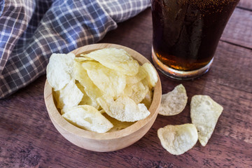 potato chips and cola in glass  on wooden table.
