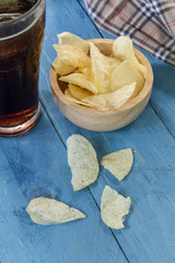 potato chips and cola in glass  on wooden table.