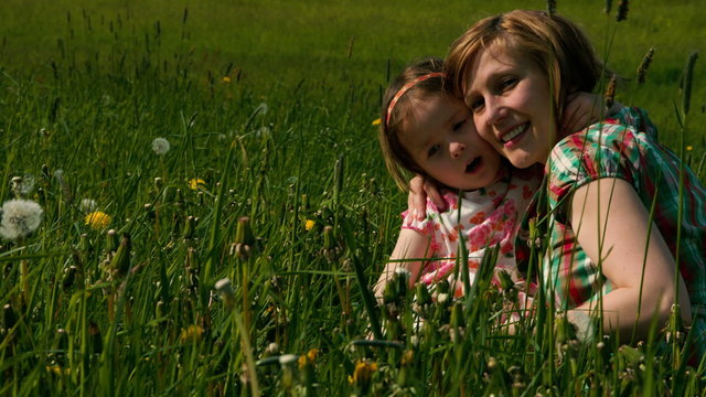 Mutter und Tochter kuscheln im Abendlicht auf einer Wiese