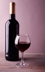 A bottle of red wine and a glass on wooden table
