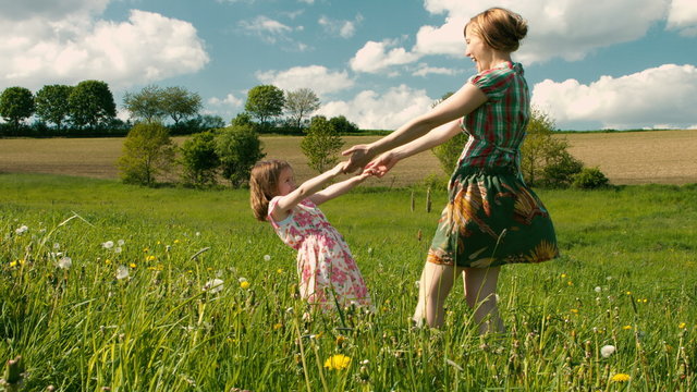 Mutter und Tochter tanzen zusammen im Wind auf einer Fr&uuml;hlingswiese