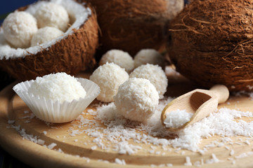 Candies in coconut flakes and fresh coconut on wooden board, close-up
