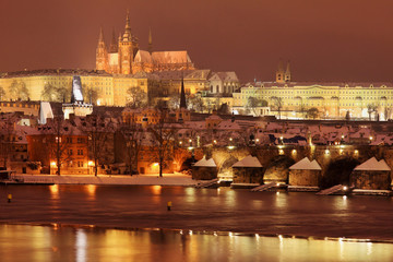 Fototapeta na wymiar Night snowy Prague gothic Castle and St. Nicholas' Cathedral with Charles Bridge, Czech republic