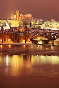 Night snowy Prague gothic Castle and St. Nicholas' Cathedral with Charles Bridge, Czech republic