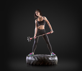 Athletic young woman doing a fitness workout with hammer and tire on black studio background