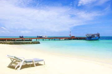 Maldives, beach with chair and dock with boat