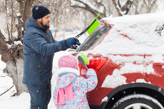 Transportation, Winter, Weather, People And Vehicle Concept - Man And Kid Cleaning Snow From Car With Brush