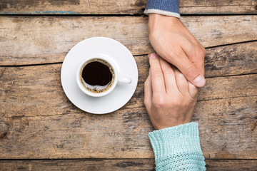 Man holds woman's hand with cup of coffee