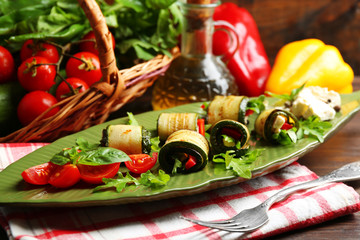Zucchini rolls with cheese, bell peppers and arugula on plate, close-up, on table background