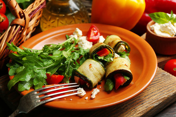 Zucchini rolls with cheese, bell peppers and arugula on plate, close-up, on table background