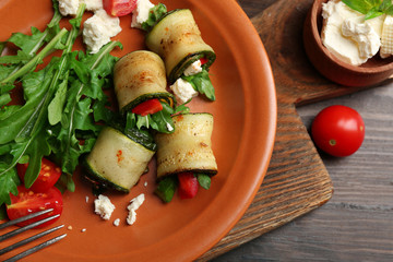 Zucchini rolls with cheese, bell peppers and arugula on plate, close-up, on table background