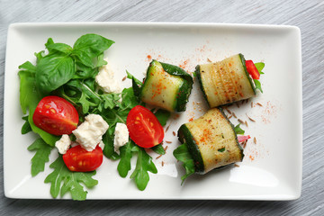 Zucchini rolls with cheese, bell peppers and arugula on plate, close-up, on table background
