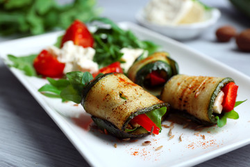 Zucchini rolls with cheese, bell peppers and arugula on plate, close-up