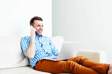 Young man making a call on his mobile and looking at the laptop