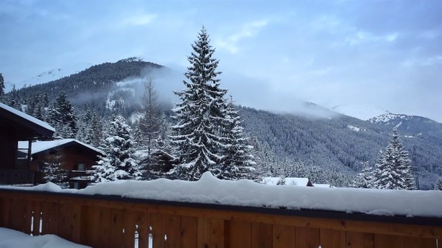 Time lapse clip of clouds moving over a snowy mountain seen from the snow covered balcony of a chalet in the mountains.