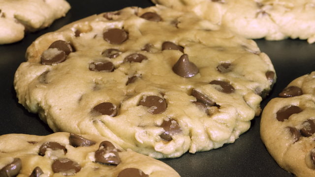 Time lapse of an extreme closeup of a chocolate chip cookie baking on a cookie sheet in an oven; progresses from raw dough to finished cookie. Shallow focus on one cookie.