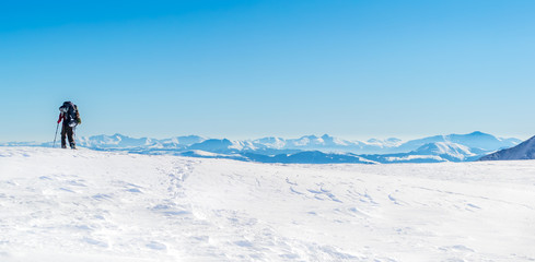 Tourist walking on snow and leaving traces. Against the background of a mountain range. Clear sky, sunny. Winter. Ukraine