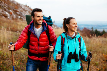 Backpackers couple hiking during fall with sticks - obrazy, fototapety, plakaty