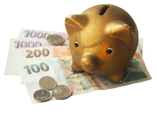 Old broken piggy bank standing on czech crown coins and banknotes. Isolated on white background. 