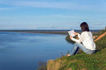 Young woman sitting on the shore of the lake with blank sheet of