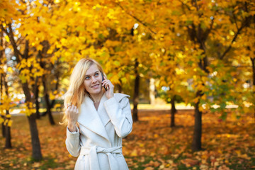 girl in white coat talking on the phone in the autumn park