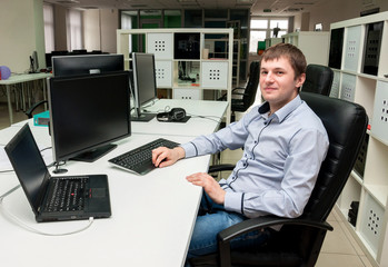 Young handsome happy man with computer in the office. Programmin