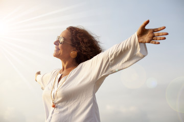 Mujer con los brazos abiertos hacia el sol radiante - obrazy, fototapety, plakaty