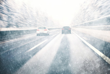 Blurry dangerous car overtaking on highway at heavy snowy conditions. Motion blur visualizies the speed and dynamics. Danger and fast speed driving at the heavy snowy and icy road. 