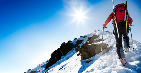Ski mountaineer walking up along a steep snowy ridge with the sk - obrazy, fototapety, plakaty