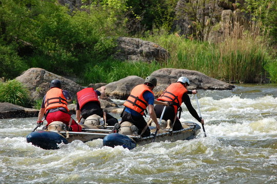 Team of people on an inflatable catamaran row up the stream in a thresholds. Southern Bug river, Ukraine.