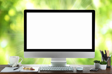 Computer on wooden table on nature green background
