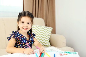 Cute little girl drawing picture on home interior background