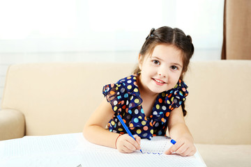 Cute little girl doing her homework, close-up, on home interior background