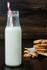 Stack of homemade chocolate chip cookies with milk on dark wooden table. Copy space background