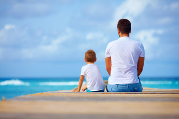father and son sitting on pier near the sea