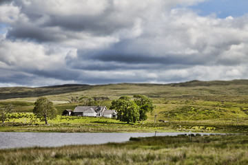 Farmhouse with tilt and shift in between clouds and stream.