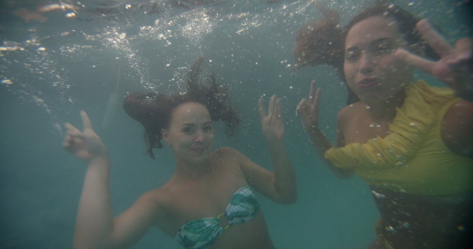 Girl friends smiling and posing happily underwater in bikinis