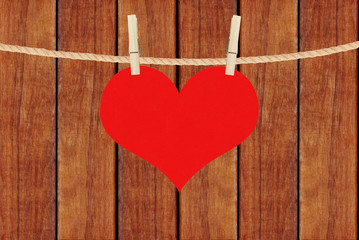 red heart hang on clothespins over brown wooden planks backgroun