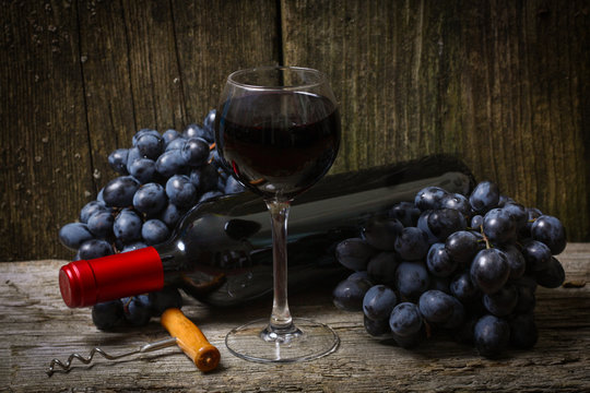 Bottle of red wine, grape and corkscrew on wooden table