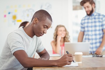 Man writing on paper while sitting at desk 