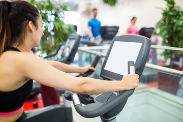 Fototapeta premium Woman on an exercise bike looking at the tv screen