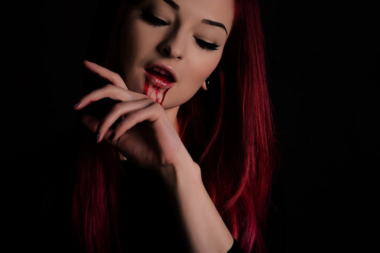Vampire woman with blood on her face and red hair against black