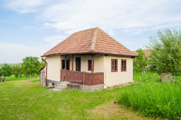 Traditional romanian rural house in Transylvania with fresh green grass and trees around on a sunny summer day with a beautifull wood porch