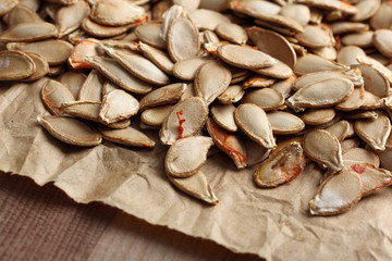 pumpkin seeds on paper on wooden background closeup
