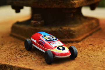 An antique race car, made before 1960s, parks on the rusty foundation of well pump.