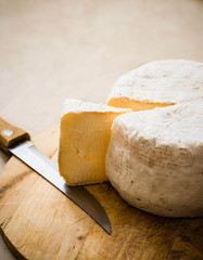 whole caciotta cheese with slice over chopping board