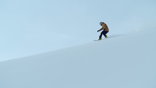 Slow motion of snowboarder riding down a snow hill and doing a powder turn 