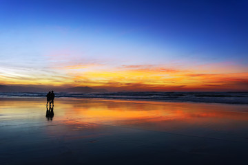 couple walking on beach at sunset - obrazy, fototapety, plakaty