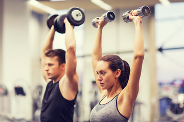 smiling man and woman with dumbbells in gym